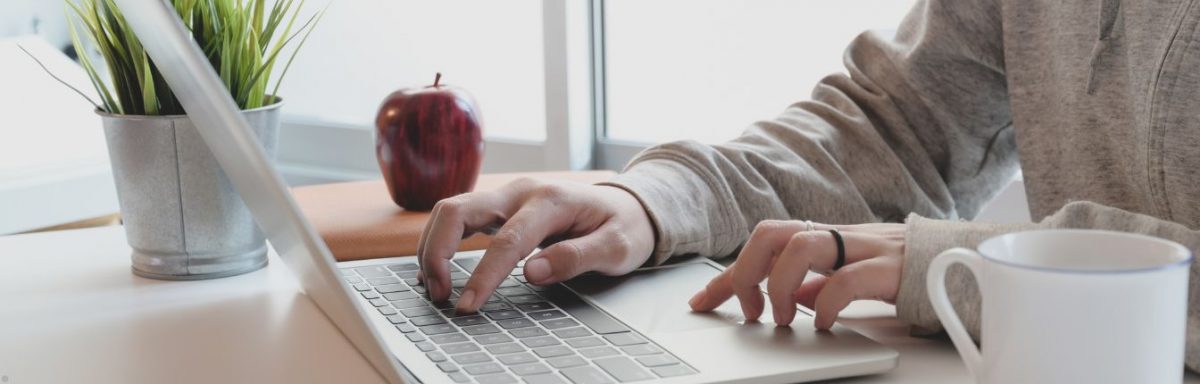 A close up shot of two hands on a laptop keyboard. It's sitting on a white desk.