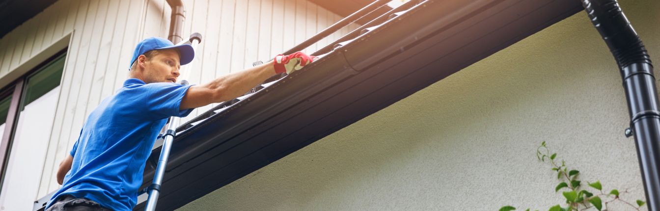 A man cleaning out a gutter on the side of a house.