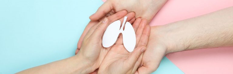 Two sets of hands holding a paper cut out of lungs against a blue and pink background.